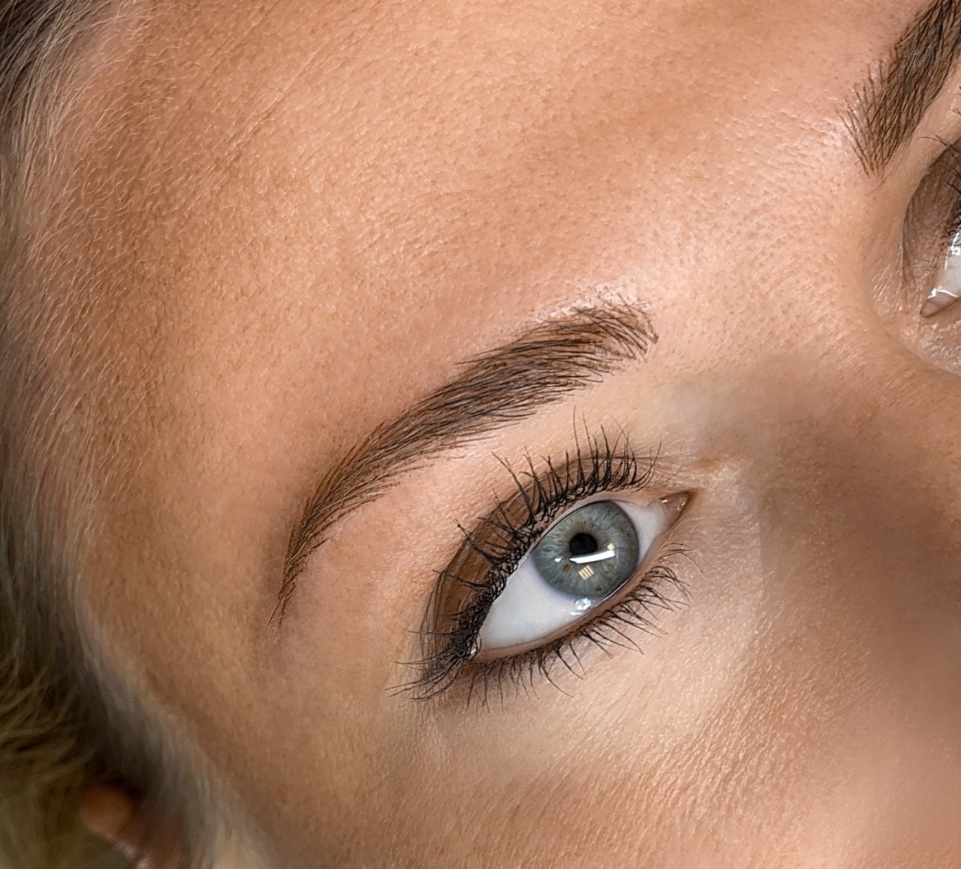 Ergebnis einer Härchenzeichnung: feine, natürliche Augenbraue über einem blauen Auge